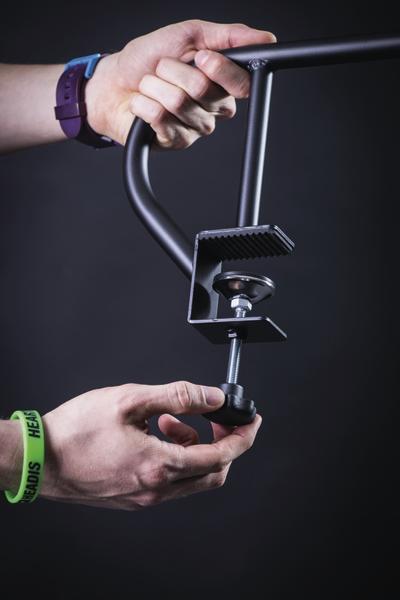 Hand hält schwarzen Metallhalter mit Schraubklemme vor dunklem Hintergrund.