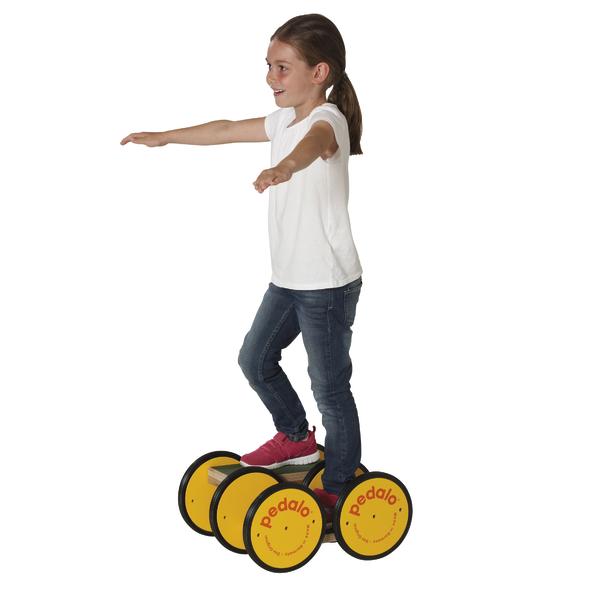 Mädchen balanciert auf gelbem Pedalo-Brett mit ausgestreckten Armen, weißes Shirt, Jeans.