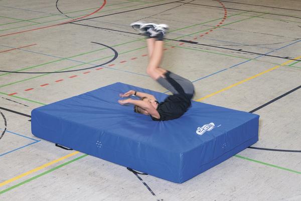 Junge macht Rückwärtsrolle auf blauem Turnmatte in Sporthalle mit Linienmarkierungen.