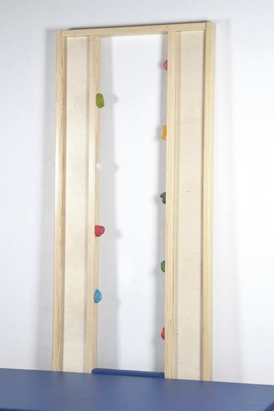Kletterwand aus Holz mit bunten Griffen und blauer Matte vor weißer Wand.