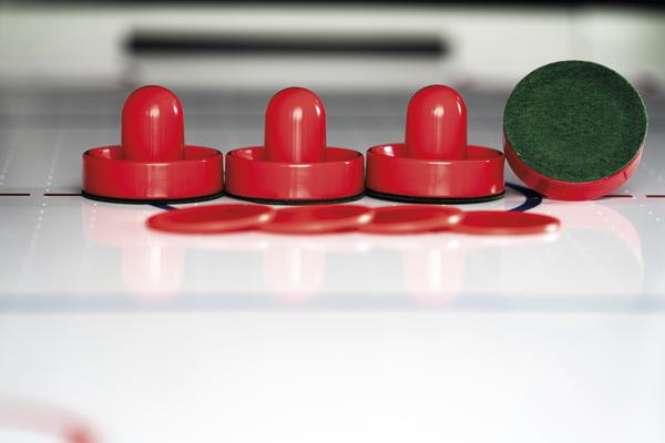 Rote Airhockey-Schläger auf einem weißen Airhockey-Tisch, einer liegt auf der Seite.