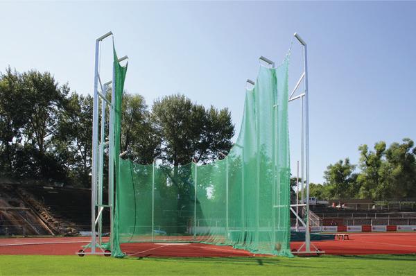 Hammerwurfkäfig mit grünem Netz auf einer Leichtathletik-Anlage bei klarem Himmel.