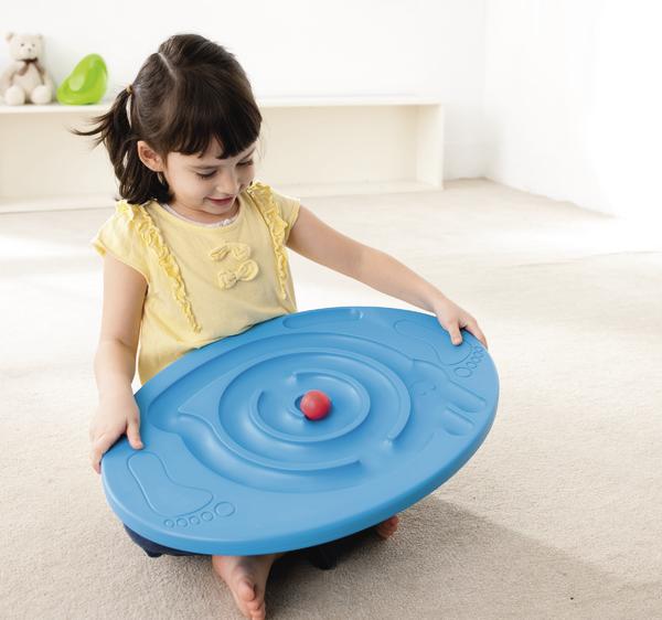 Kind spielt mit blauem Balancierbrett und rotem Ball auf hellem Teppichboden.