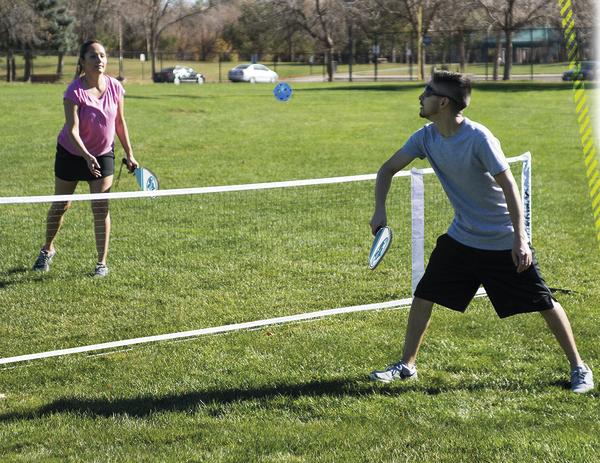 Junge und Mädchen spielen Badminton im Park auf grünem Rasen bei Sonnenschein.