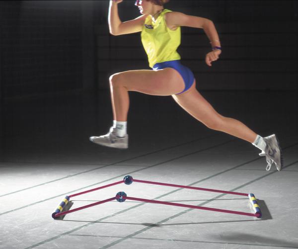 Frau springt im Sportoutfit über ein Trainingshindernis in der Halle.