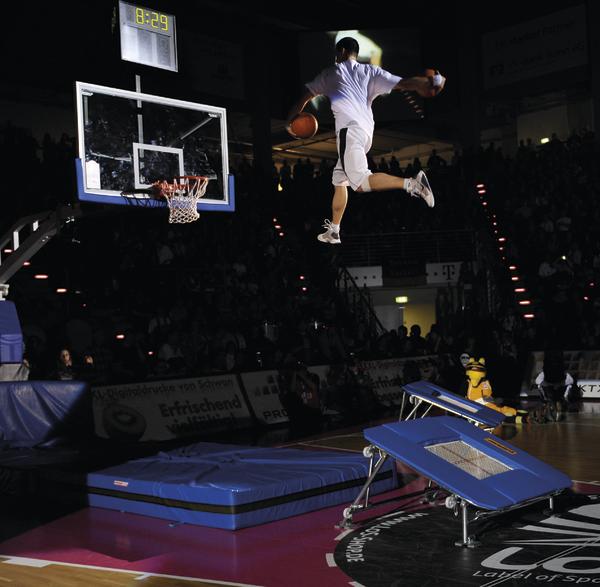 Basketballspieler springt mit Ball über Trampolin zum Korb in Halle bei Dunk Show.