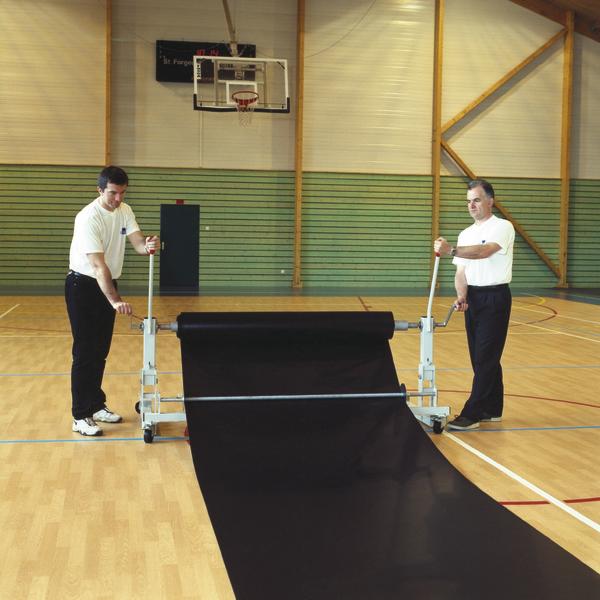 Zwei Männer rollen eine schwarze Schutzmatte in einer Sporthalle mit Basketballkorb aus.