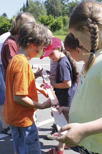 Kinder spielen draußen ein Teamspiel mit Holzteilen und Bällen an einem sonnigen Tag.