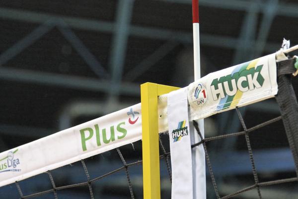 Volleyballnetz mit Plus und Huck Sponsorenlogos in einer Sporthalle.