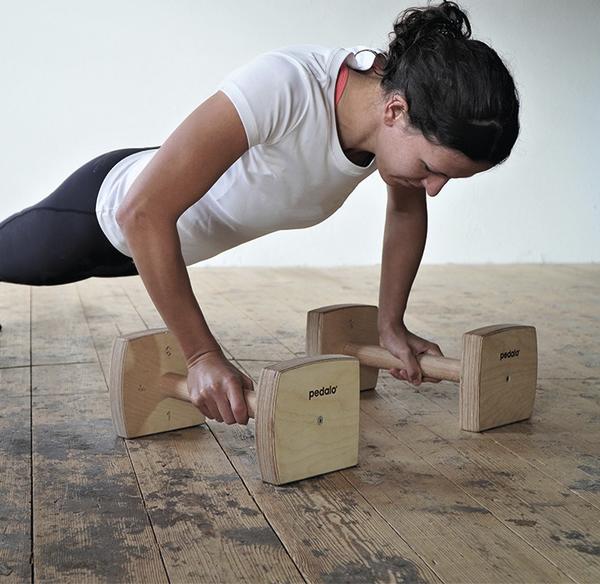 Frau macht Liegestütze mit Holzgriffen auf Holzboden für Krafttraining und Fitness.