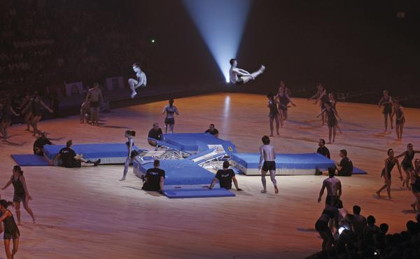 Akrobaten springen auf Trampolinen bei einer Indoor-Turnshow mit Bühnenbeleuchtung.
