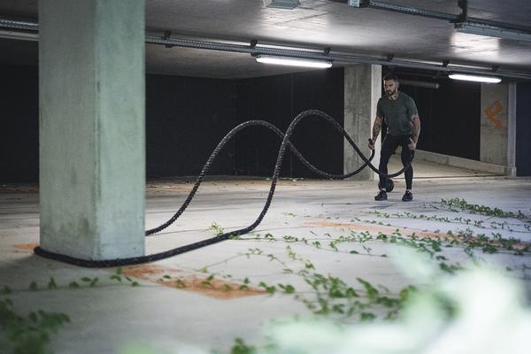 Mann trainiert mit Battle Ropes in einer dunklen, urbanen Tiefgarage für Kraft und Ausdauer.