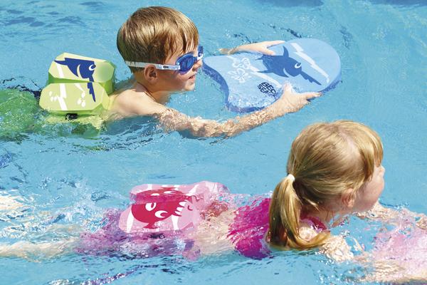 Kinder schwimmen mit Schwimmflügeln und Schwimmbrettern im Pool.
