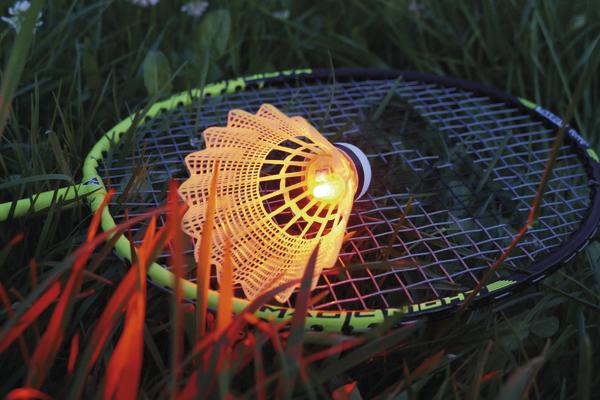 Leuchtender Badminton-Schläger und Federball im Gras bei Dämmerung.