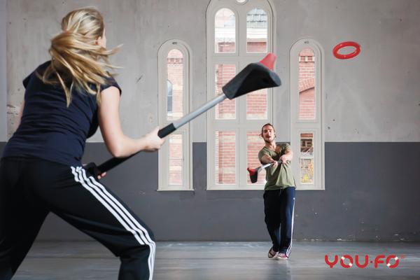 Frau und Mann spielen in Halle mit Wurfschläger und Frisbee-Scheibe.