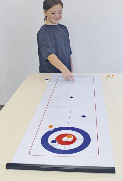 Kind spielt Tisch-Curling auf weißem Spielbrett mit Zielscheibe und Spielsteinen.