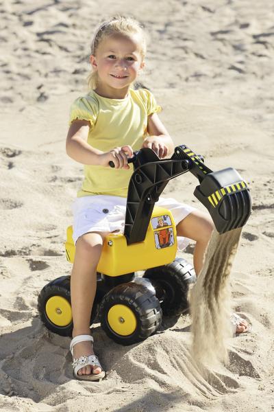 Kind spielt mit gelbem Spielzeugbagger im Sand und schaufelt Sand aus.