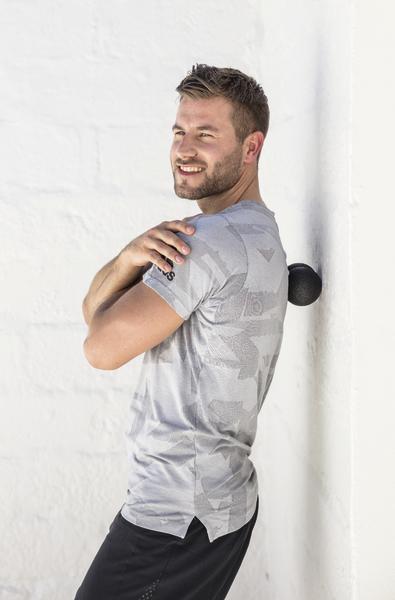 Mann nutzt Massageball an der Wand zur Muskelentspannung im Rückenbereich.