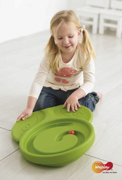 Kleines Mädchen spielt mit grünem Labyrinth-Spielzeug auf hellem Boden, Weplay-Logo sichtbar.