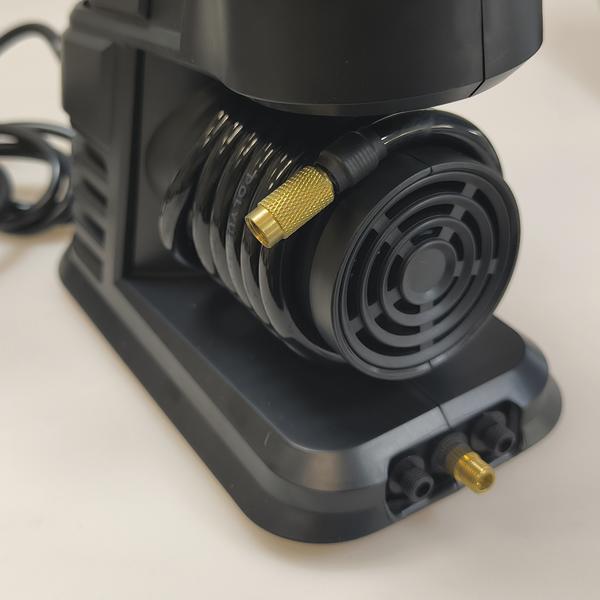 Nahaufnahme eines schwarzen Kompressors mit angeschlossenem Schlauch und goldfarbenem Ventiladapter auf der Vorderseite.