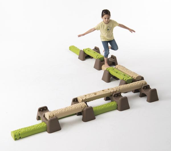 Kind balanciert auf grün-beigen Balancierbalken aus Kunststoff auf weißem Hintergrund.