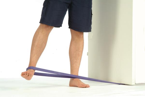 Mann trainiert Fußmuskulatur mit Widerstandsband an Tür befestigt, barfuß.