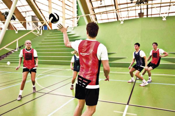 Volleyballspiel in der Halle mit Spielern in roten und schwarzen Trikots beim Aufschlag.