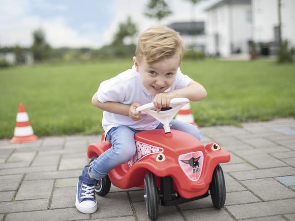 Kleiner Junge fährt fröhlich Bobby-Car auf gepflastertem Weg im Freien.