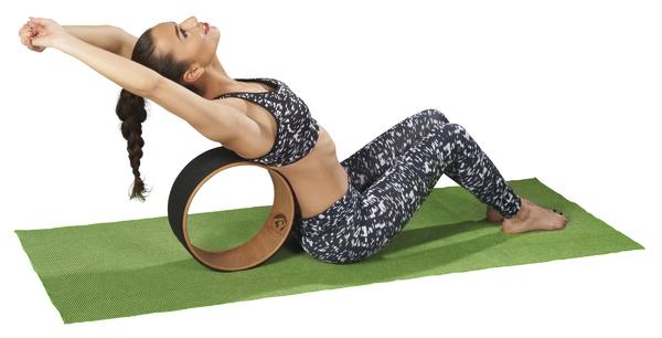 Frau dehnt Rücken auf Yogarad auf grüner Matte, trägt Sportoutfit, Fitness und Entspannung.