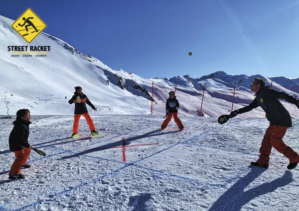 Vier Personen spielen Street Racket auf schneebedecktem Berg mit blauem Himmel.