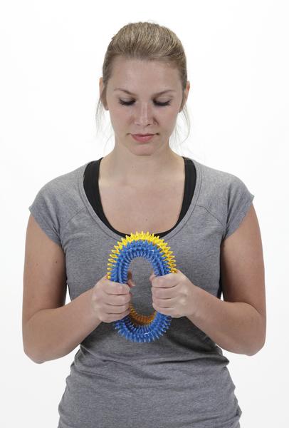 Frau hält bunten Handtrainer zur Finger- und Handmuskelstärkung vor weißem Hintergrund.