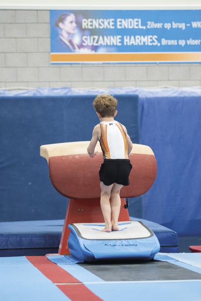 Junge beim Turnen auf Sprungtisch in Sporthalle mit Werbebanner im Hintergrund.