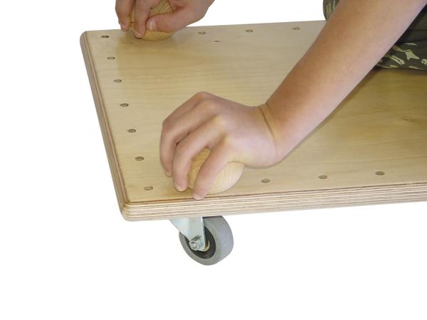 Kind spielt mit Holzspielzeug auf fahrbarem Holzbrett mit Rollen, motorische Förderung.