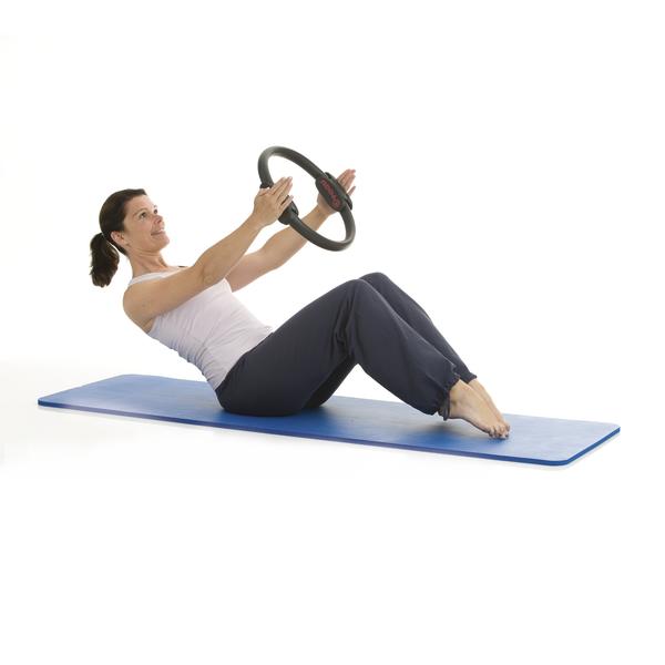 Frau macht Pilates-Übung mit Pilates-Ring auf blauer Matte vor weißem Hintergrund.