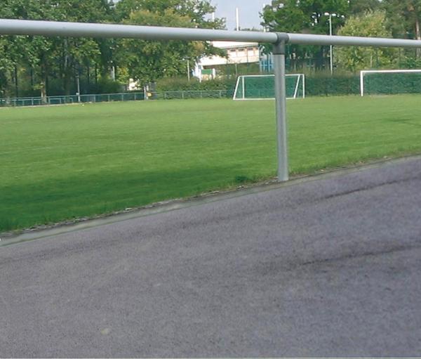 Fußballplatz mit grünem Rasen, Toren und umlaufendem Laufweg bei Tageslicht.