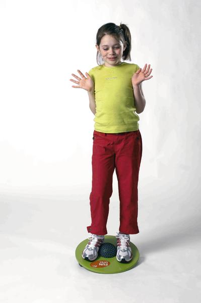 Mädchen balanciert auf grünem Balance-Board, trägt grüne Bluse und rote Hose.