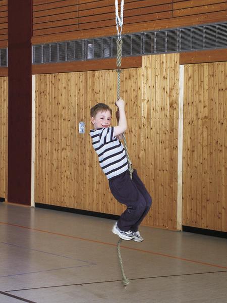 Junge schwingt an einem Seil in einer Turnhalle mit Holzwänden.