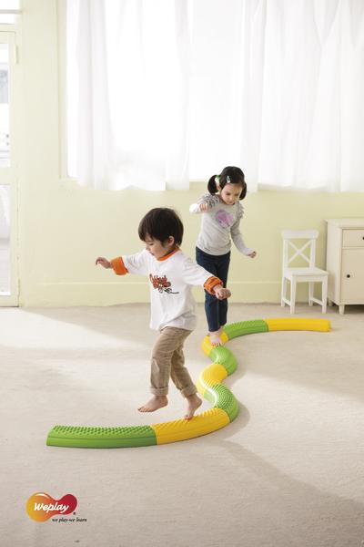 Kinder balancieren auf buntem Wackelpfad im hellen Raum für motorische Förderung.