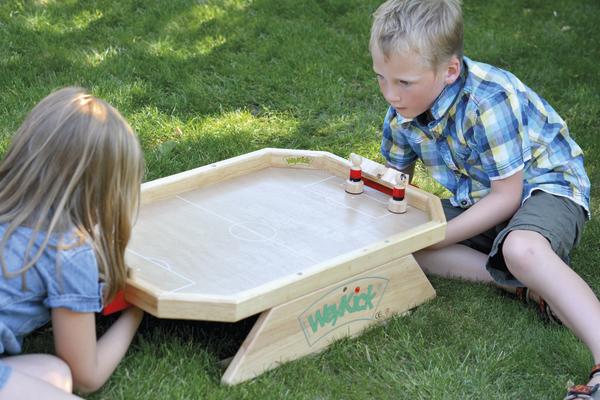 Kinder spielen draußen auf dem Rasen ein Holz-Tischspiel mit kleinen Figuren.
