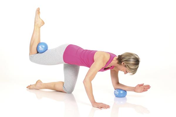 Frau macht Pilates-Übung mit blauen Bällen zur Kräftigung von Rücken und Beinen.