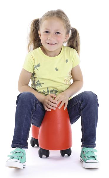 Kind mit Zöpfen sitzt lachend auf rotem Rollhocker, trägt gelbes Shirt und blaue Jeans.