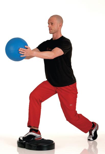 Mann macht Ausfallschritt mit Medizinball auf Balancekissen für Stabilitätstraining.