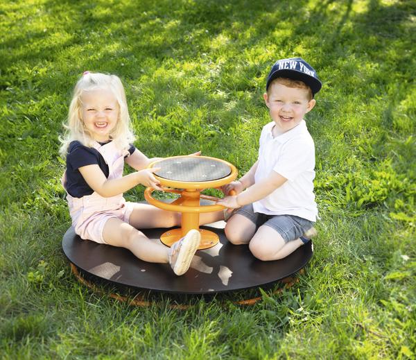 Zwei lachende Kinder spielen auf einem Karussell im sonnigen Park auf grünem Gras.
