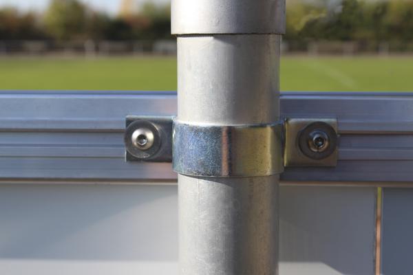 Metallhalterung befestigt ein Rohr an einem Aluminiumrahmen vor grünem Hintergrund.