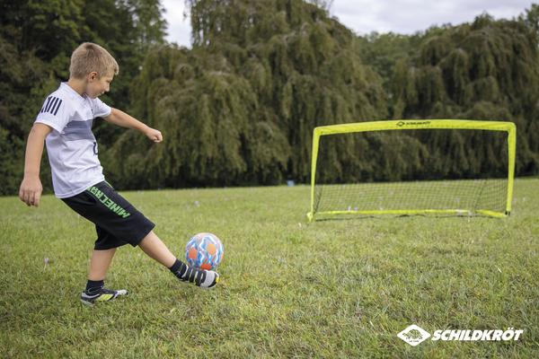Junge schießt Fußball auf kleines Tor im Garten, Outdoor-Sport für Kinder.