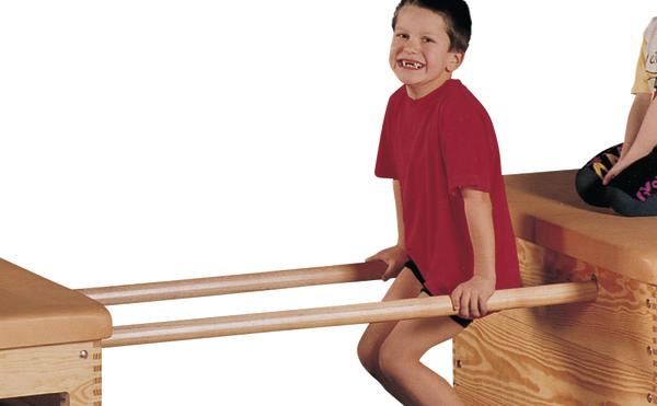 Junge in rotem Shirt sitzt lachend auf Holzstangen zwischen zwei Holzkästen beim Spielen.