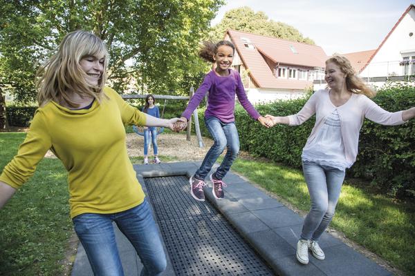Drei Mädchen springen lachend gemeinsam auf einem Gartentrampolin im Freien.