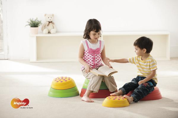 Kinder sitzen auf bunten Sitzkissen und lesen gemeinsam ein Buch in hellem Raum.