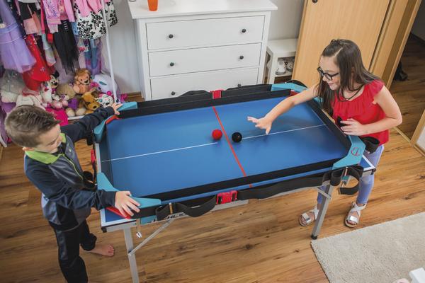 Kinder spielen Tischhockey auf einem blauen Spieltisch in einem Kinderzimmer.