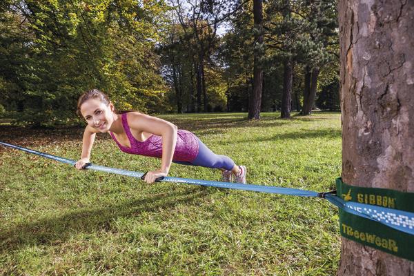 Frau trainiert Balance und Kraft auf Slackline im Park bei sonnigem Wetter.